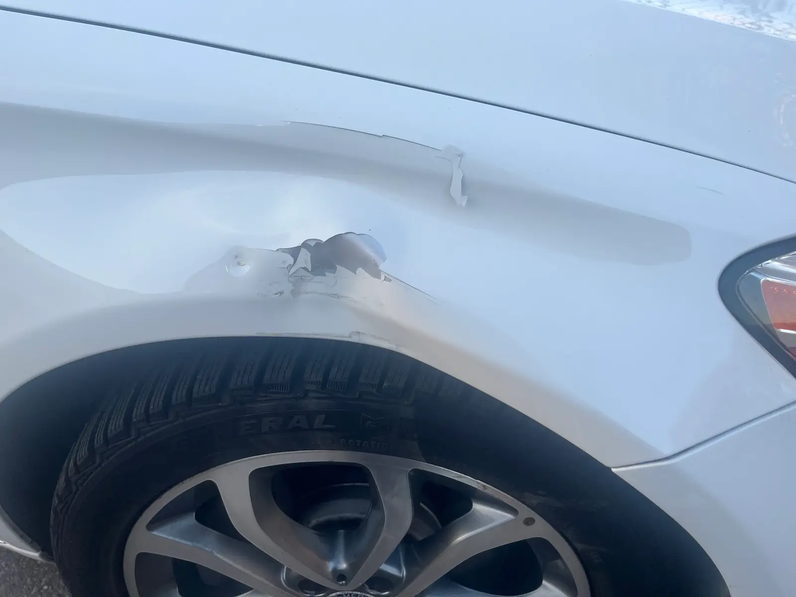 White car with a dented rear quarter panel and paint damage before repair